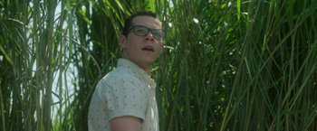 Movie still from “In the Tall Grass” (2019), directed by Vincenzo Natali – A young man wearing glasses standing in front of tall grass; Close Up shot, Low angle