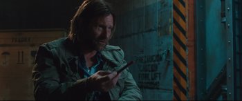 Movie still from “Incarnate” (2016), directed by Brad Peyton – A man holding a cell phone while standing in a room; Medium shot, Over the shoulder angle