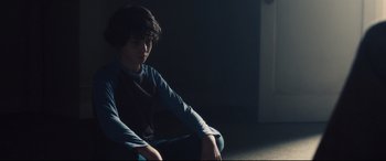 Movie still from “Incarnate” (2016), directed by Brad Peyton – A young man sitting in a dark room with his hands crossed; Medium shot, High angle