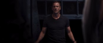 Movie still from “Incarnate” (2016), directed by Brad Peyton – A man in a black t - shirt stands in front of a window; Medium shot, Over the shoulder angle
