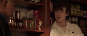 Movie still from “Kaleidoscope” (2023), directed by Mairzee Almas – A man standing next to a shelf in a room; Close Up shot, Over the shoulder angle