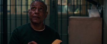 Movie still from “Kaleidoscope” (2023), directed by Mairzee Almas – An older man holding a book in front of a fence; Close Up shot, Over the shoulder angle