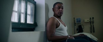 Movie still from “Kaleidoscope” (2023), directed by Mairzee Almas – An older man in a white tank top is chained to a wall; Medium shot, Low angle