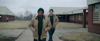 Movie still from “Kaleidoscope” (2023), directed by Mairzee Almas – Two men in green hats and jackets walking down a street; Medium shot, Low angle