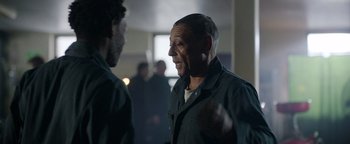 Movie still from “Kaleidoscope” (2023), directed by Mairzee Almas – Two men are talking in a room; Medium shot, Over the shoulder angle