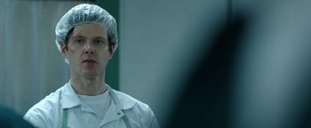 Movie still from “Kaleidoscope” (2023), directed by Mairzee Almas – A man wearing a white lab coat and head covering; Close Up shot, Over the shoulder angle