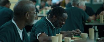 Movie still from “Kaleidoscope” (2023), directed by Mairzee Almas – A man sitting at a table with a cup of coffee; Medium shot, High angle