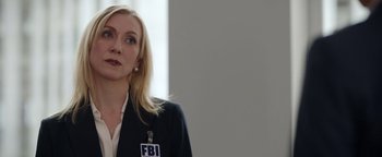 Movie still from “Kaleidoscope” (2023), directed by Mairzee Almas – A woman wearing a fbi badge stands in front of a white wall; Close Up shot, Over the shoulder angle