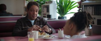 Movie still from “Kaleidoscope” (2023), directed by Mairzee Almas – A man sitting at a table eating a sandwich; Close Up shot, Over the shoulder angle