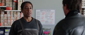 Movie still from “Kaleidoscope” (2023), directed by Mairzee Almas – A man standing in front of a sign that says service rates; Medium shot, Over the shoulder angle