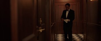 Movie still from “Kaleidoscope” (2023), directed by Mairzee Almas – A man in a tuxedo standing next to a door way; Medium shot, Low angle