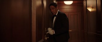 Movie still from “Kaleidoscope” (2023), directed by Mairzee Almas – A man in a tuxedo and white gloves opening the door of a hotel room; Medium shot, Low angle