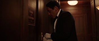 Movie still from “Kaleidoscope” (2023), directed by Mairzee Almas – A man in a suit and white gloves opening the door of a hotel room; Medium shot, Low angle