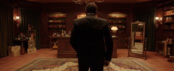 Movie still from “Kaleidoscope” (2023), directed by Mairzee Almas – A man in a suit standing in front of a desk; Medium shot, Low angle