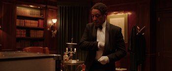 Movie still from “Kaleidoscope” (2023), directed by Mairzee Almas – A man in a suit and tie holding a white glove; Medium shot, Over the shoulder angle