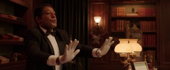 Movie still from “Kaleidoscope” (2023), directed by Mairzee Almas – A man in a black suit and white gloves holding a lamp; Medium shot, Low angle