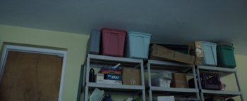 Movie still from “Kaleidoscope” (2023), directed by Mairzee Almas – A room with a shelf with a lot of boxes on top of it; Medium shot, Low angle