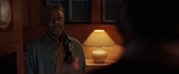 Movie still from “Kaleidoscope” (2023), directed by Mairzee Almas – An older man holding a gun in front of a lamp; Close Up shot, Over the shoulder angle