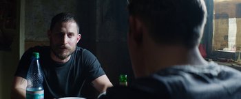 Movie still from “Kidnapping Stella” (2019), directed by Thomas Sieben – Two men are sitting at a table and one of them is holding a bottle; Close Up shot, Over the shoulder angle