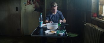 Movie still from “Kidnapping Stella” (2019), directed by Thomas Sieben – A man sitting at a table with a plate of food; Medium shot, High angle