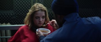 A woman is eating soup from a bowl while a man watches