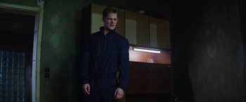 Movie still from “Kidnapping Stella” (2019), directed by Thomas Sieben – A young man in a black suit standing in front of a cabinet; Medium shot, Low angle