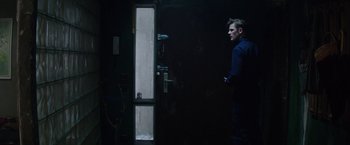 Movie still from “Kidnapping Stella” (2019), directed by Thomas Sieben – A man standing next to a door in a dark room; Medium shot, Low angle