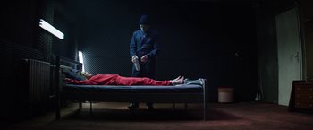 Movie still from “Kidnapping Stella” (2019), directed by Thomas Sieben – A man standing next to a person laying on a bed; Wide shot, High angle