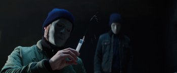 Movie still from “Kidnapping Stella” (2019), directed by Thomas Sieben – Two men in a dark room one is holding a syringe and the other is wearing a blue hat; Close Up shot, Low angle