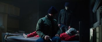 Movie still from “Kidnapping Stella” (2019), directed by Thomas Sieben – A man sitting on a bed with another man laying on the ground; Medium shot, Low angle