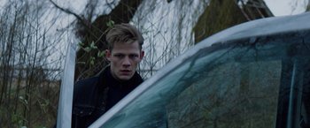 Movie still from “Kidnapping Stella” (2019), directed by Thomas Sieben – A man standing in front of a car in a wooded area; Close Up shot, Over the shoulder angle