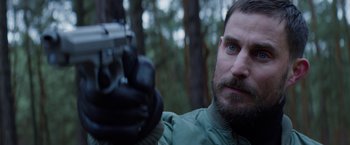 Movie still from “Kidnapping Stella” (2019), directed by Thomas Sieben – A person holding a gun with trees in the background; Close Up shot, Over the shoulder angle