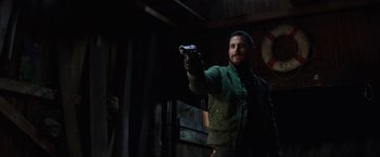 Movie still from “Kidnapping Stella” (2019), directed by Thomas Sieben – A man holding a gun while standing next to a wall; Medium shot, Over the shoulder angle