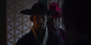 Movie still from “Kingdom” (2019), created by Eun-hee Kim – A man wearing a hat standing next to another man wearing a hat; Close Up shot, Over the shoulder angle