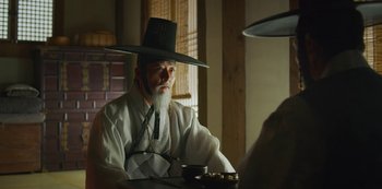 Movie still from “Kingdom” (2019), created by Eun-hee Kim – An old man wearing a hat sitting at a table; Close Up shot, Over the shoulder angle