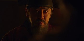 Movie still from “Kingdom” (2019), created by Eun-hee Kim – A man with a beard wearing a hat and holding an umbrella; Close Up shot, Low angle