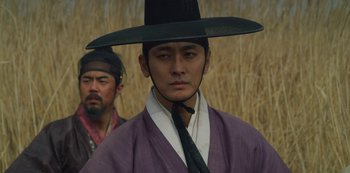 Movie still from “Kingdom” (2019), created by Eun-hee Kim – A man wearing a black hat and a purple robe; Close Up shot, Low angle