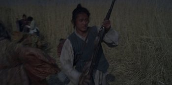 Movie still from “Kingdom” (2019), created by Eun-hee Kim – A man holding a rifle while sitting in a field; Medium shot, Low angle