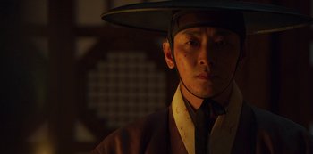 Movie still from “Kingdom” (2019), created by Eun-hee Kim – A man wearing a hat and a suit; Close Up shot, Low angle