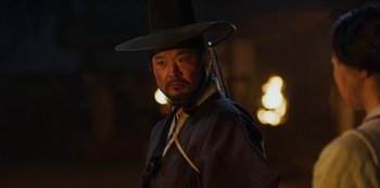 Movie still from “Kingdom” (2019), created by Eun-hee Kim – A man wearing a black hat and holding a sword; Close Up shot, Low angle