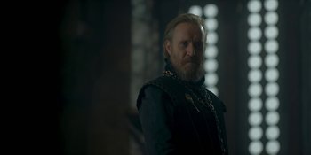 Movie still from “House of the Dragon” (2022), created by George R.R. Martin – A man with long hair and a goatee standing in a dark room; Medium shot, Low angle