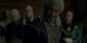 Movie still from “House of the Dragon” (2022), created by George R.R. Martin – A man with a long dreadlocks wearing a black and gold outfit; Close Up shot, Over the shoulder angle