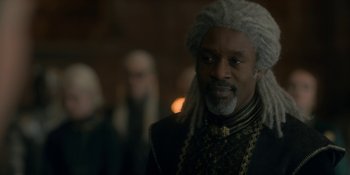 Movie still from “House of the Dragon” (2022), created by George R.R. Martin – A man with long white dreadlocks is looking at the camera; Close Up shot, Over the shoulder angle