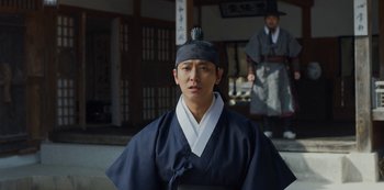Movie still from “Kingdom” (2019), created by Eun-hee Kim – A man wearing a black hat and a black robe; Medium shot, Over the shoulder angle