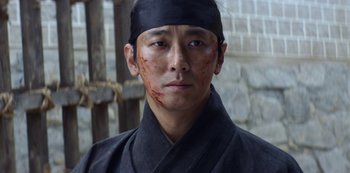 Movie still from “Kingdom” (2019), created by Eun-hee Kim – A man in a black shirt and a black hat with blood all over his face; Close Up shot, Low angle