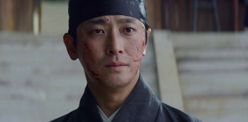 Movie still from “Kingdom” (2019), created by Eun-hee Kim – A person wearing a hat with blood on his face; Close Up shot, Low angle