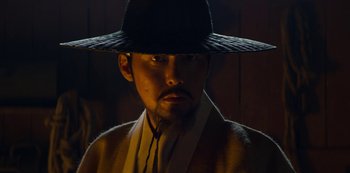 Movie still from “Kingdom” (2019), created by Eun-hee Kim – A man wearing a black hat and a yellow jacket; Close Up shot, Low angle