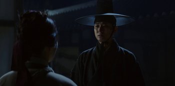 Movie still from “Kingdom” (2019), created by Eun-hee Kim – A man wearing a black hat standing next to a woman; Close Up shot, Over the shoulder angle