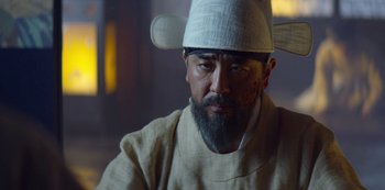 Movie still from “Kingdom” (2019), created by Eun-hee Kim – A man with a beard wearing a white hat; Close Up shot, Low angle