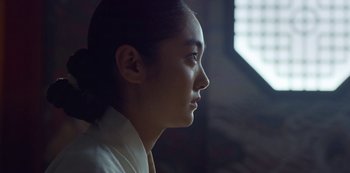 Movie still from “Kingdom” (2019), created by Eun-hee Kim – A young asian woman looking out a window; Close Up shot, Low angle